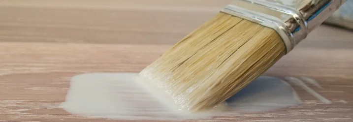 Pinsel trägt weiße Farbe auf Holz auf